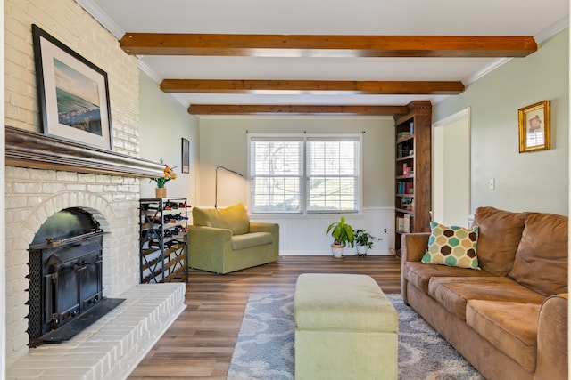 living room featuring beamed ceiling, wood-type flooring, ornamental molding, and a fireplace