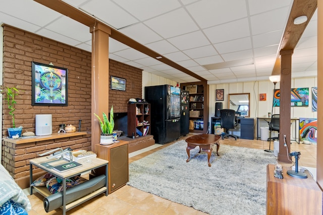 living room featuring light tile patterned flooring, brick wall, and a drop ceiling