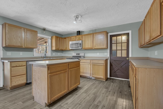 kitchen with sink, a center island, a textured ceiling, appliances with stainless steel finishes, and light wood-type flooring