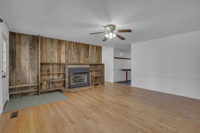 unfurnished living room featuring ceiling fan, wooden walls, and light hardwood / wood-style flooring