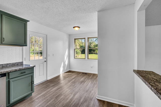 interior space with a textured ceiling, green cabinets, stainless steel dishwasher, and dark hardwood / wood-style floors