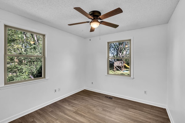 empty room with a textured ceiling, ceiling fan, a healthy amount of sunlight, and dark hardwood / wood-style floors