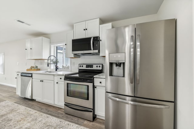 kitchen featuring white cabinetry, sink, light hardwood / wood-style flooring, decorative backsplash, and appliances with stainless steel finishes