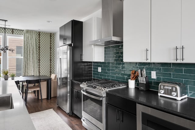 kitchen with dark wood-type flooring, white cabinets, wall chimney exhaust hood, decorative backsplash, and appliances with stainless steel finishes