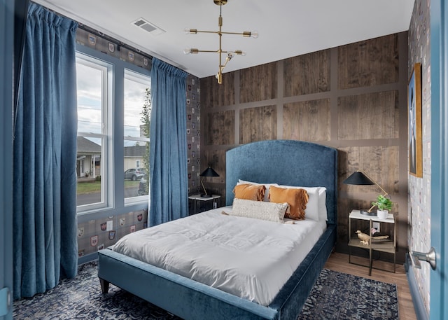 bedroom featuring wood walls, wood-type flooring, and a chandelier