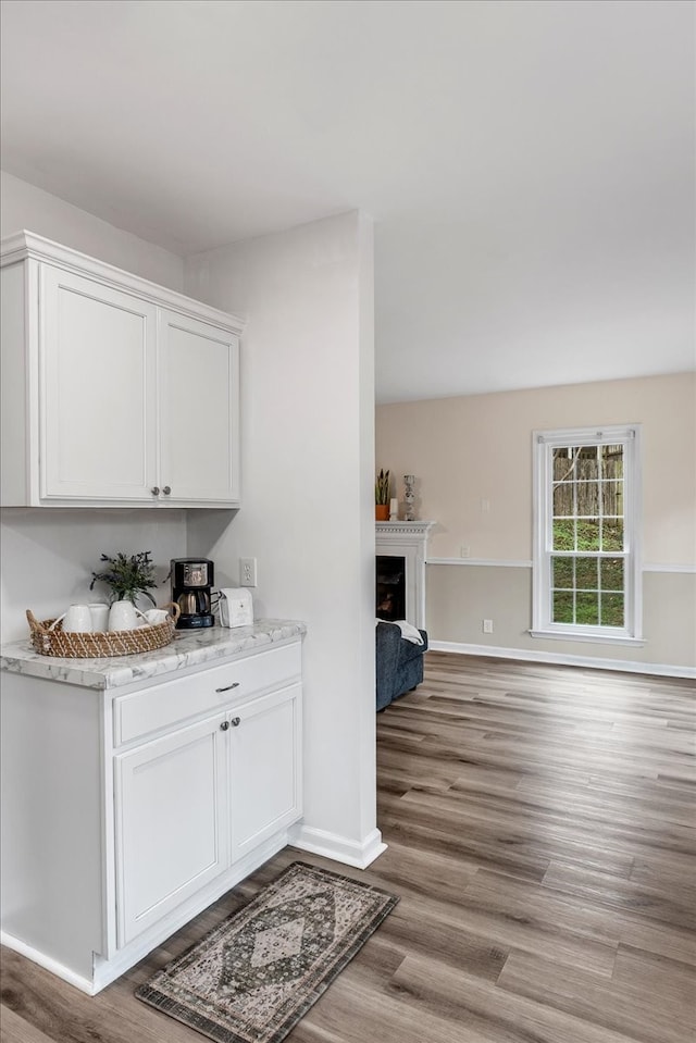 bar with white cabinets, light hardwood / wood-style floors, and light stone counters