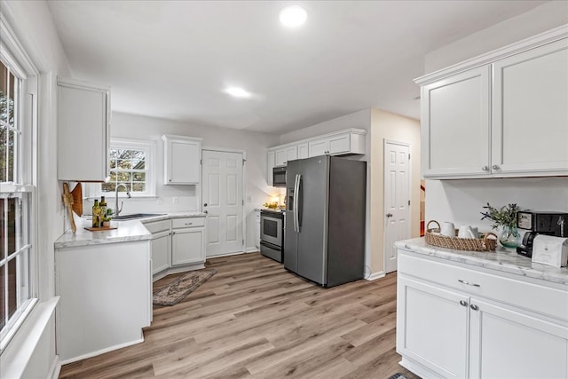 kitchen featuring light stone countertops, stainless steel appliances, sink, white cabinets, and light hardwood / wood-style floors