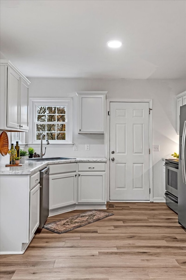 kitchen featuring appliances with stainless steel finishes, light hardwood / wood-style flooring, white cabinetry, and sink