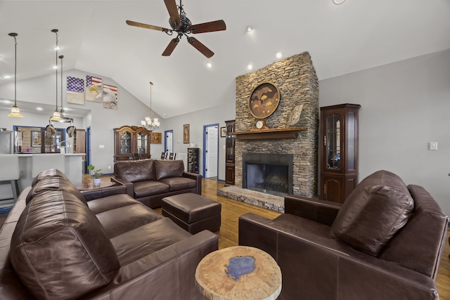 living room with ceiling fan with notable chandelier, hardwood / wood-style flooring, a stone fireplace, and high vaulted ceiling