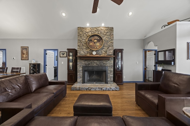 living room with a stone fireplace, ceiling fan, vaulted ceiling, and hardwood / wood-style flooring