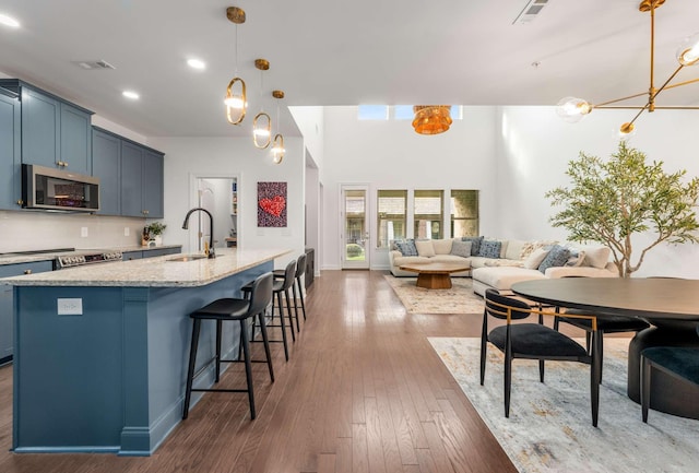 kitchen with blue cabinets, dark wood-type flooring, sink, a center island with sink, and hanging light fixtures