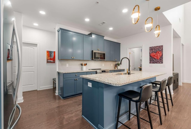 kitchen featuring stainless steel appliances, dark wood-type flooring, sink, decorative light fixtures, and a center island with sink