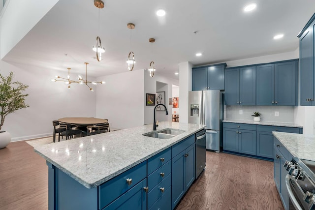 kitchen with appliances with stainless steel finishes, a center island with sink, blue cabinets, and dark hardwood / wood-style floors