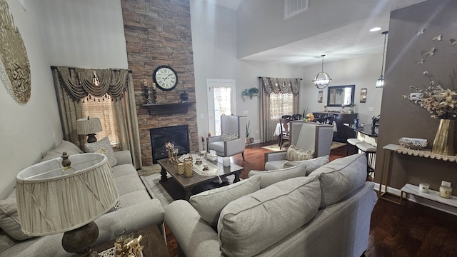 living room featuring hardwood / wood-style floors, a stone fireplace, a high ceiling, and a chandelier