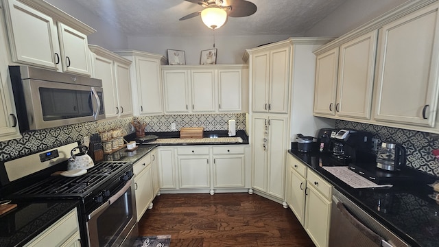 kitchen with stainless steel appliances, dark hardwood / wood-style flooring, dark stone countertops, cream cabinets, and decorative backsplash