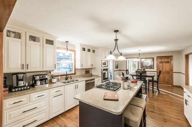 kitchen featuring appliances with stainless steel finishes, light wood-type flooring, sink, decorative light fixtures, and a kitchen island