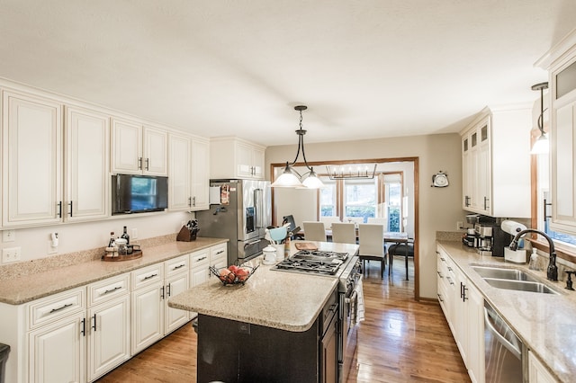 kitchen with appliances with stainless steel finishes, sink, light hardwood / wood-style flooring, a center island, and hanging light fixtures