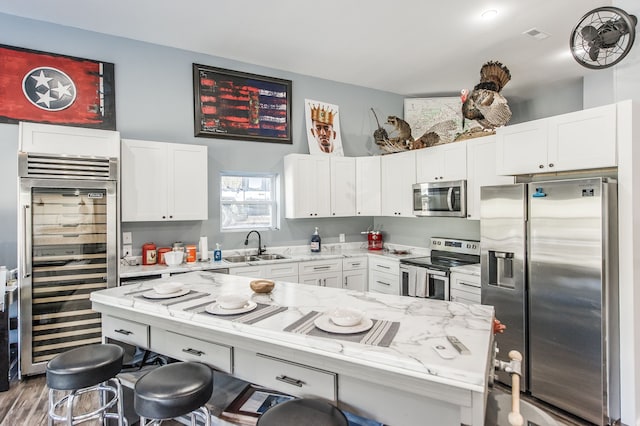 kitchen with light stone counters, stainless steel appliances, beverage cooler, sink, and white cabinets