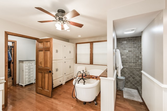 bathroom with a bathing tub, ceiling fan, wood-type flooring, and tile walls