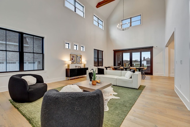 living room featuring beam ceiling, light hardwood / wood-style flooring, a healthy amount of sunlight, and a high ceiling