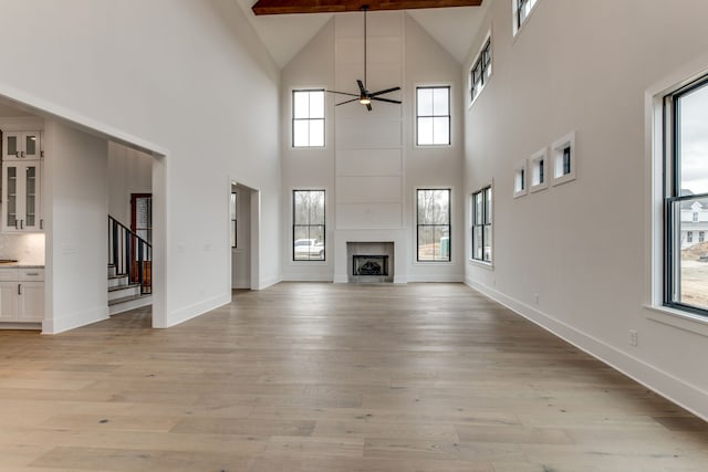 unfurnished living room with ceiling fan, beam ceiling, light wood-type flooring, and a towering ceiling