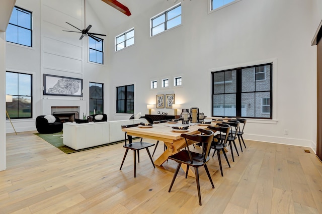 dining space featuring ceiling fan, light wood-type flooring, and a high ceiling