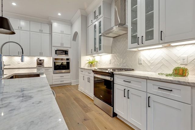 kitchen featuring wall chimney range hood, sink, tasteful backsplash, decorative light fixtures, and stainless steel appliances