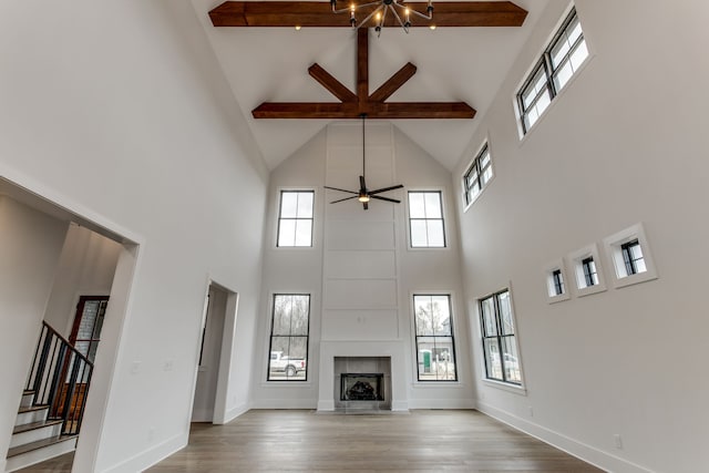 unfurnished living room featuring a tile fireplace, light hardwood / wood-style flooring, ceiling fan, a towering ceiling, and beam ceiling