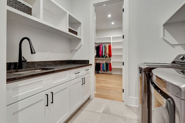 washroom featuring washing machine and clothes dryer, sink, light tile patterned floors, and cabinets