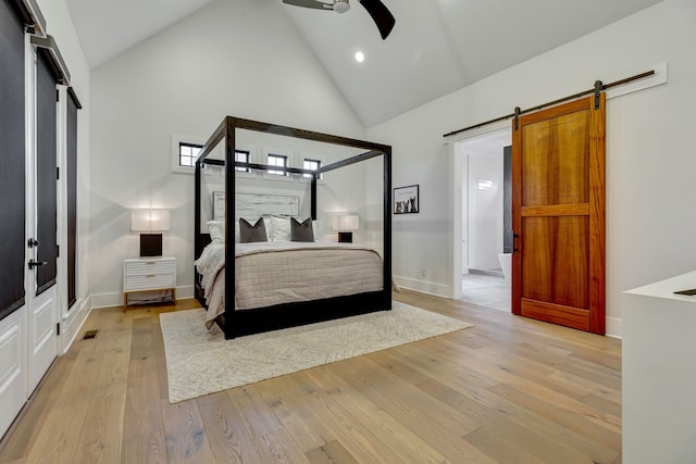 bedroom featuring ceiling fan, a barn door, high vaulted ceiling, and light hardwood / wood-style flooring