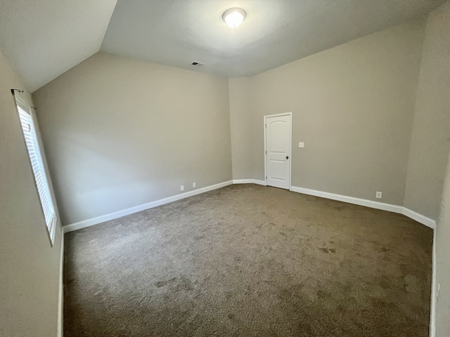 spare room with lofted ceiling and dark colored carpet