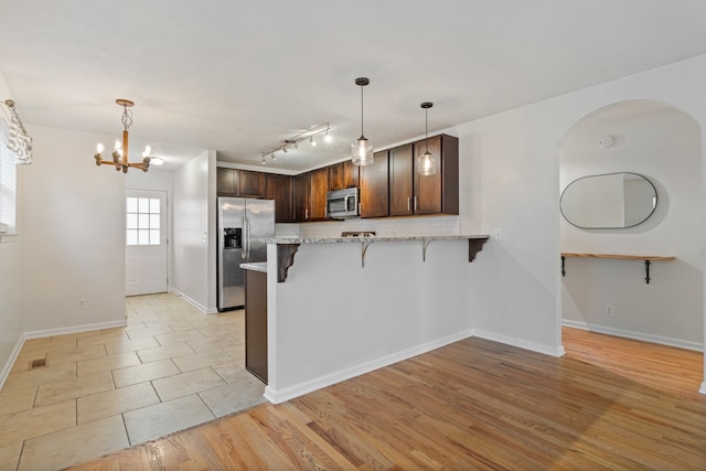 kitchen featuring appliances with stainless steel finishes, dark brown cabinets, light hardwood / wood-style floors, kitchen peninsula, and a breakfast bar area