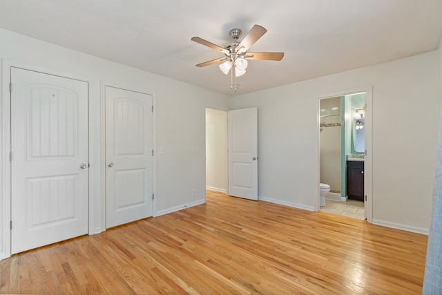 unfurnished bedroom featuring two closets, light hardwood / wood-style flooring, ensuite bath, and ceiling fan