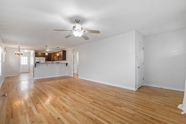 unfurnished living room featuring ceiling fan with notable chandelier and light wood-type flooring