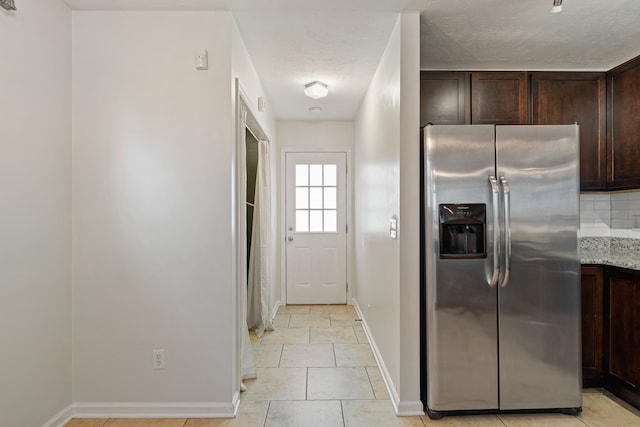 kitchen with dark brown cabinetry, light stone counters, stainless steel refrigerator with ice dispenser, backsplash, and light tile patterned floors