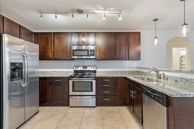 kitchen featuring kitchen peninsula, light stone counters, stainless steel appliances, sink, and hanging light fixtures