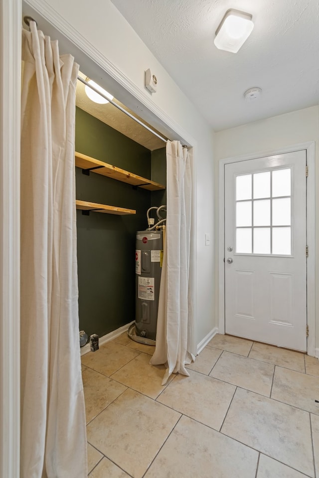 doorway to outside with electric water heater, light tile patterned floors, and a textured ceiling