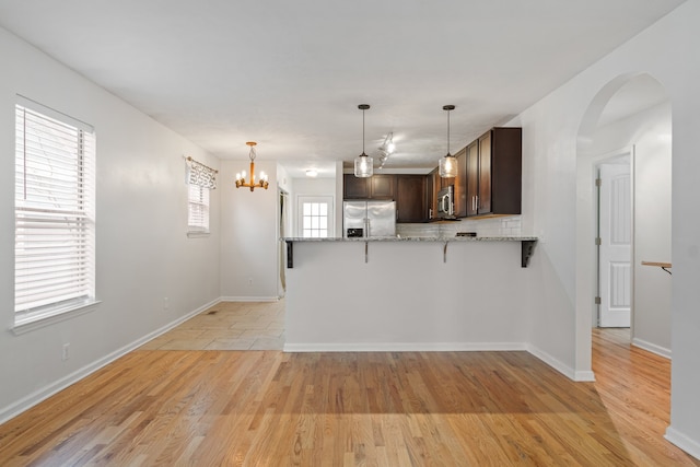 kitchen with dark brown cabinetry, light stone counters, kitchen peninsula, appliances with stainless steel finishes, and light wood-type flooring