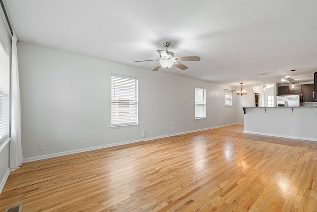 empty room with ceiling fan with notable chandelier and light hardwood / wood-style floors