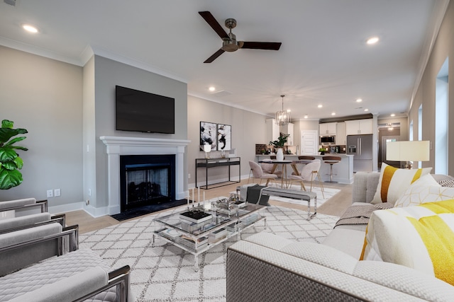 living room featuring ceiling fan with notable chandelier, light wood-type flooring, and crown molding