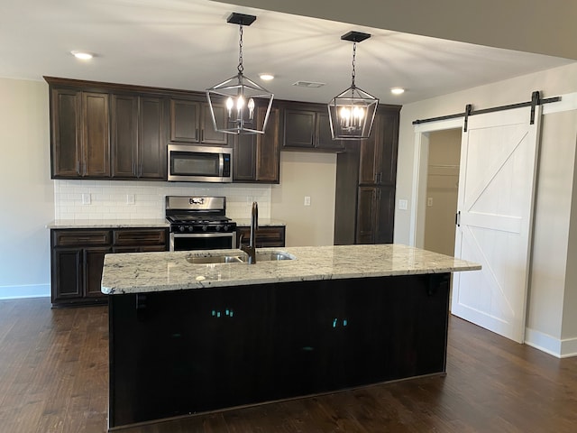 kitchen with a barn door, sink, an island with sink, and stainless steel appliances