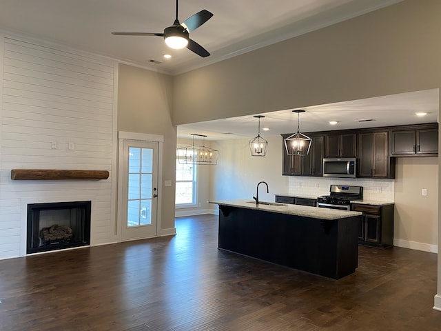 kitchen with pendant lighting, stainless steel appliances, a kitchen island with sink, and sink