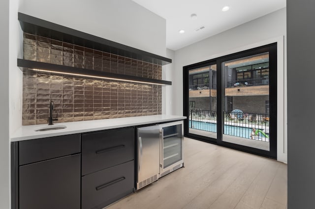 bar with stainless steel refrigerator, sink, beverage cooler, and light hardwood / wood-style floors