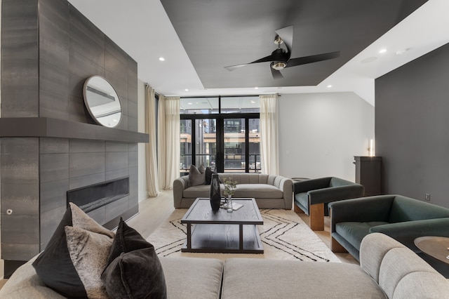 living room featuring a tile fireplace, ceiling fan, and a wall of windows