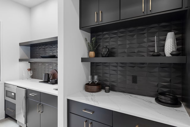 bar with decorative backsplash, stainless steel fridge, and light stone countertops