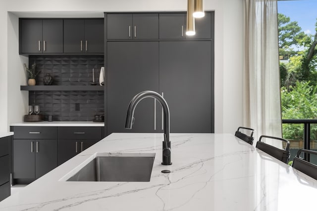 kitchen with pendant lighting, decorative backsplash, sink, and light stone countertops