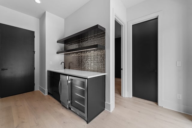 bar featuring decorative backsplash, light wood-type flooring, wine cooler, and sink