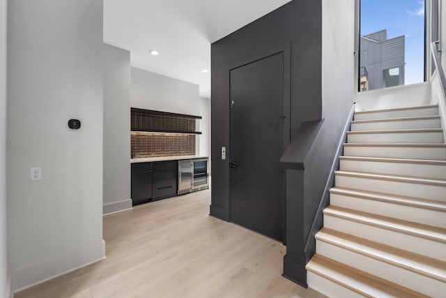 stairs featuring wood-type flooring, beverage cooler, and bar area