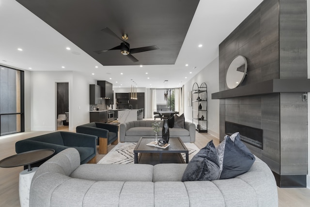 living room with a tile fireplace, light wood-type flooring, and ceiling fan