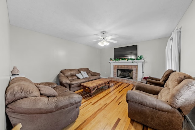 living room featuring ceiling fan, wood-type flooring, and a brick fireplace